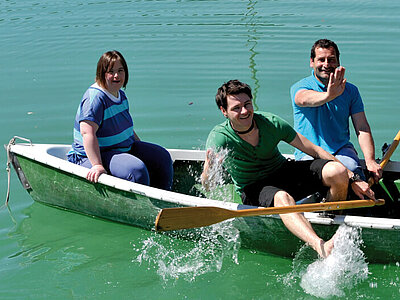  Drei Menschen mit und ohne Behinderung haben Spaß auf einem Paddelboot im Wasser