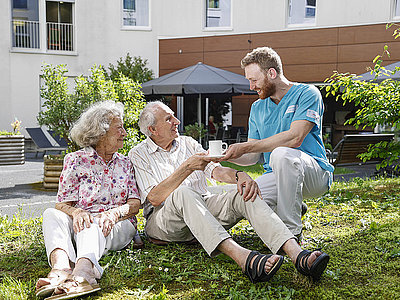 Ein älteres Paar sitzt im Garten eines Senioren-Heimes und ein Mitarbeiter bringt dem Paar Kaffee. Ein älteres Paar sitzt im Garten eines Senioren-Heimes und ein Mitarbeiter bringt dem Paar Kaffee.