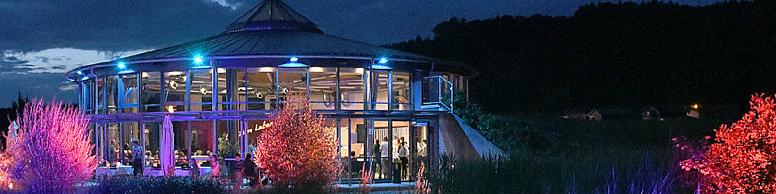 Abendstimmung am Herzogsägmühler See mit festlich erleuchtetem Rainer-Endisch-Saal im Hintergrund.