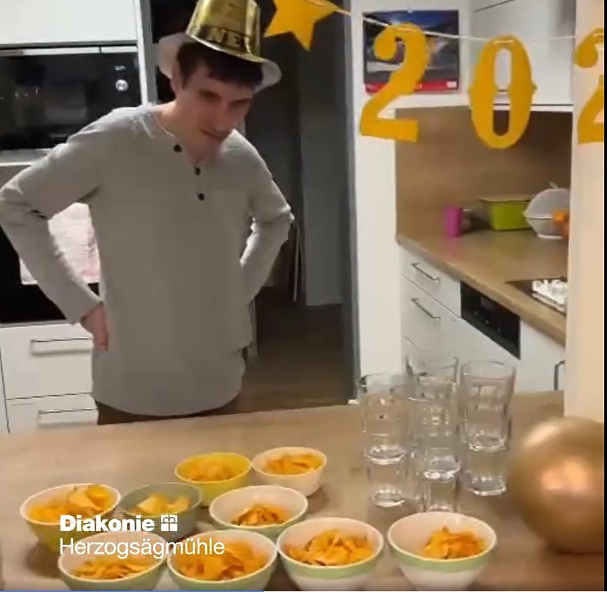 Person hinter einem Tisch, auf dem Gläser und vorbereitete Schüsselchen mit Kartoffelchips stehen.