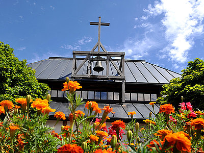 Die Dachkonstruktion mit Glockengebälk der Martinskirche, eingerahmt von Bäumen und bunten Blumen.