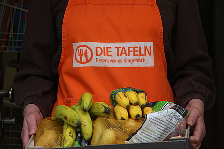 Eine Helferin der Tafel trägt eine Kiste mit Obst und Gemüse