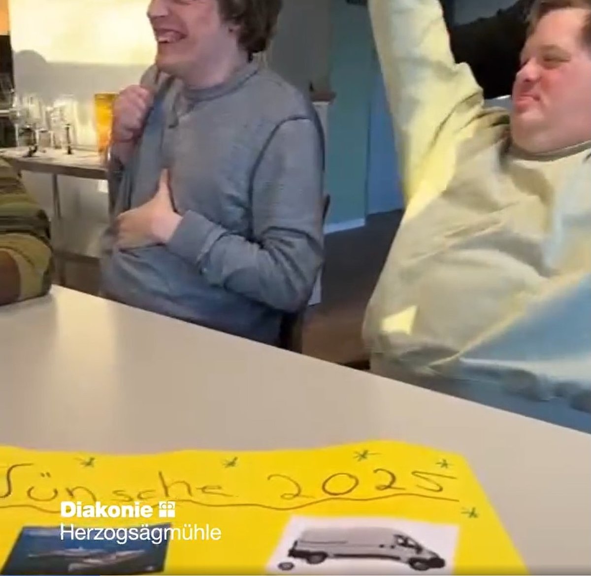 Feiernde am Tisch. Auf dem Tisch liegt ein Plakat mit Fotos, die Wünsche für 2025 symbolisieren.
