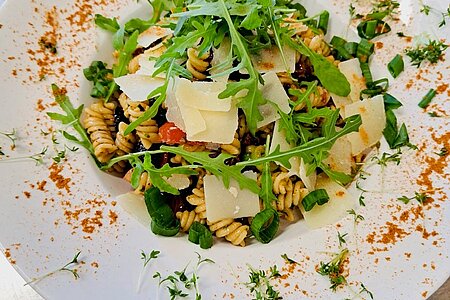 Nudelsalat mit Parmesanhobeln und Ruccola auf liebevoll dekoriertem Teller.