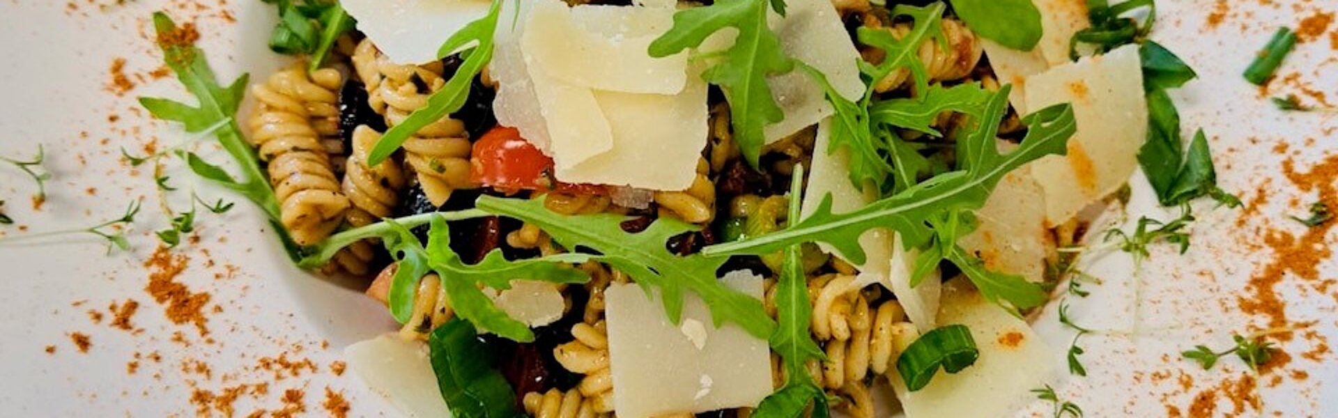 Nudelsalat mit Parmesanhobeln und Ruccola auf liebevoll dekoriertem Teller.