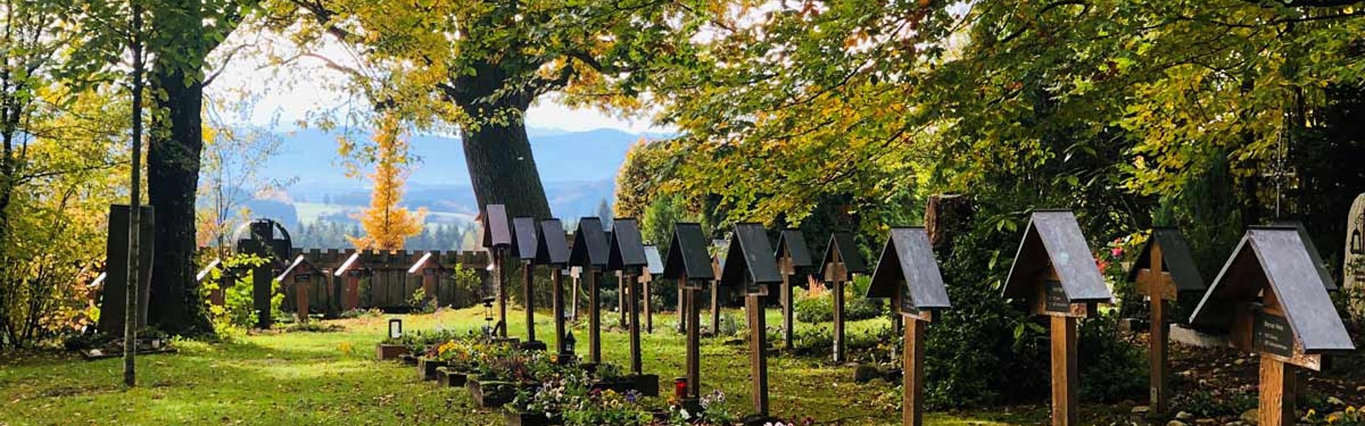 Blick von der Friedhofswiese in die Berge. Auf der Wiese sind Grabreihen mit Holzgrabkreuzen.